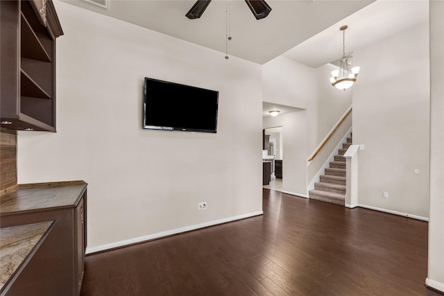 unfurnished living room with dark wood-type flooring and ceiling fan with notable chandelier