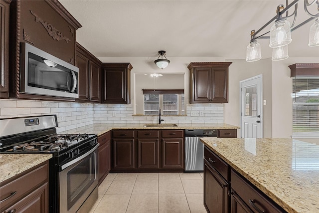 kitchen featuring appliances with stainless steel finishes, decorative light fixtures, sink, light tile patterned floors, and light stone countertops