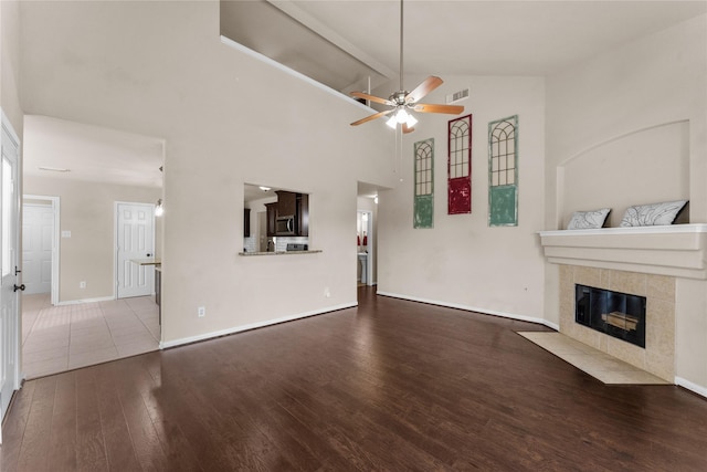 unfurnished living room with high vaulted ceiling, wood-type flooring, a tiled fireplace, ceiling fan, and beam ceiling