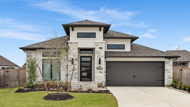 prairie-style house with an attached garage, fence, stone siding, driveway, and roof with shingles