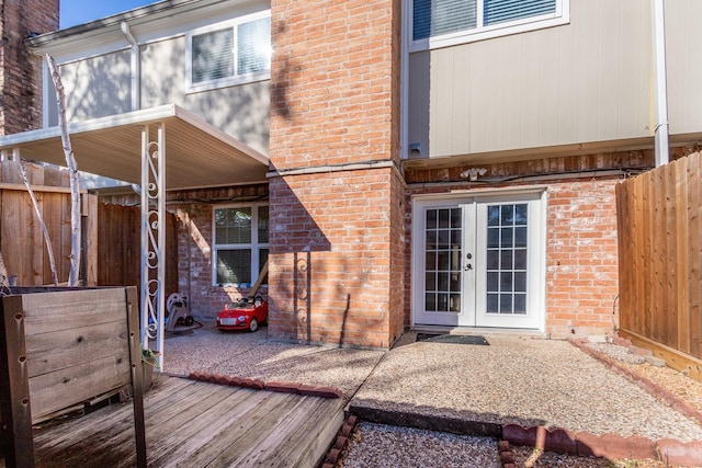 view of exterior entry featuring brick siding, a patio area, fence, and french doors