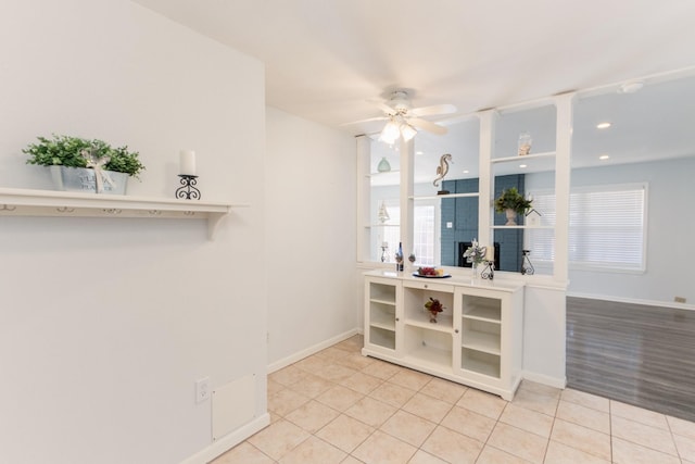 interior space with a ceiling fan, light tile patterned flooring, a fireplace, and baseboards