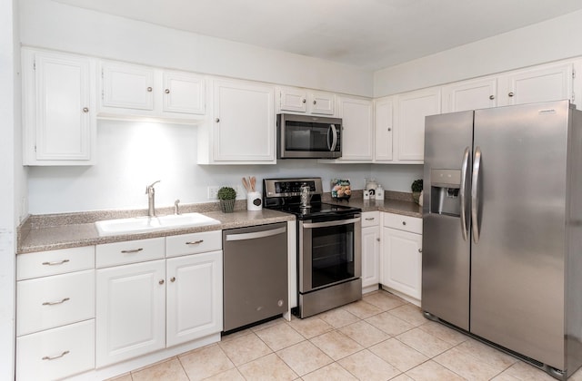 kitchen with light tile patterned flooring, appliances with stainless steel finishes, sink, and white cabinets