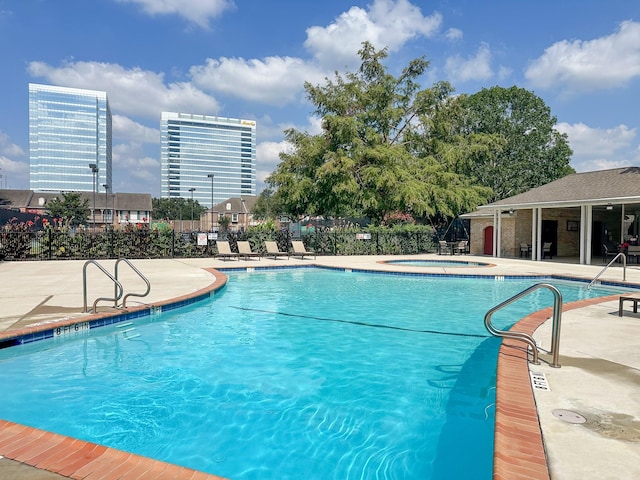 pool with a hot tub, fence, a city view, and a patio