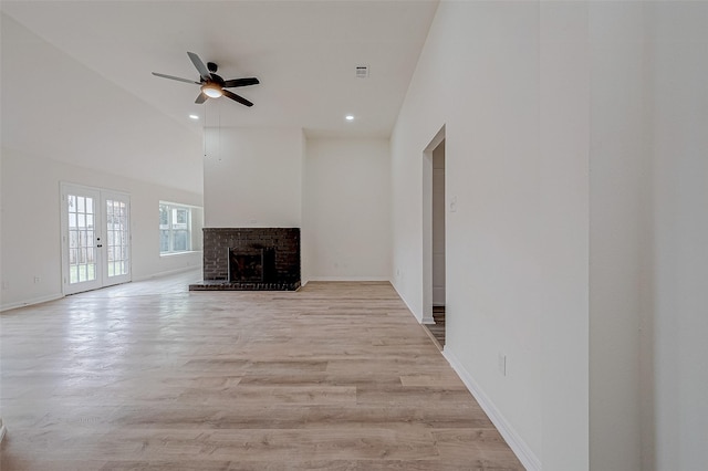 unfurnished living room featuring ceiling fan, high vaulted ceiling, a fireplace, light hardwood / wood-style floors, and french doors