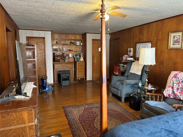 living room featuring crown molding, a wood stove, ceiling fan, dark hardwood / wood-style floors, and wood walls