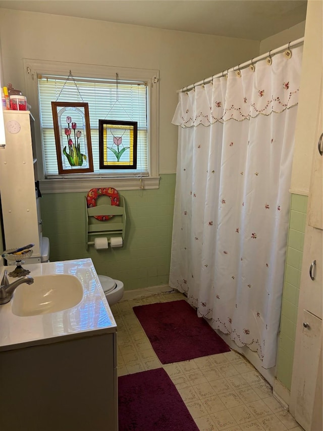 bathroom featuring walk in shower, vanity, toilet, and tile walls