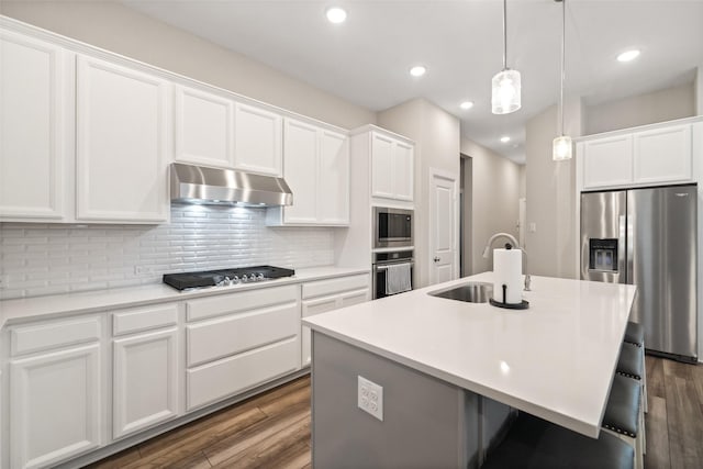 kitchen featuring under cabinet range hood, decorative backsplash, dark wood-style flooring, stainless steel appliances, and a sink