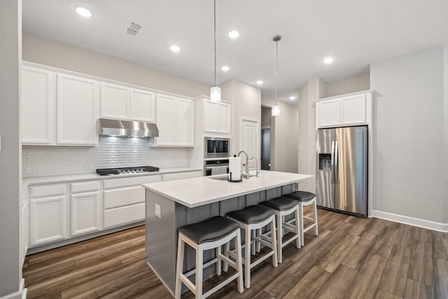 kitchen with pendant lighting, stainless steel appliances, white cabinets, and a center island with sink