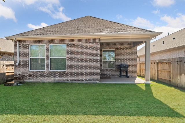 rear view of house with brick siding, a lawn, a shingled roof, and fence