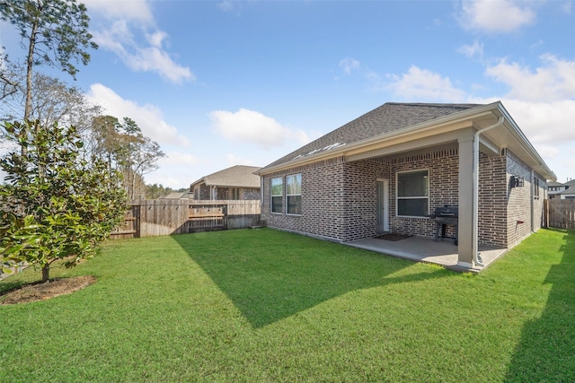 rear view of property featuring brick siding, a patio area, a yard, and a fenced backyard