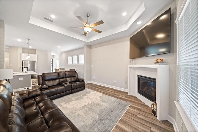 living room featuring visible vents, a ceiling fan, a tray ceiling, and wood finished floors