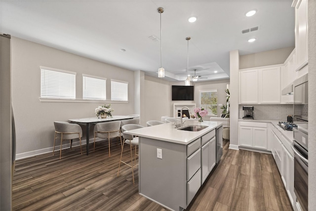 kitchen featuring visible vents, ceiling fan, a warm lit fireplace, dark wood-type flooring, and a sink