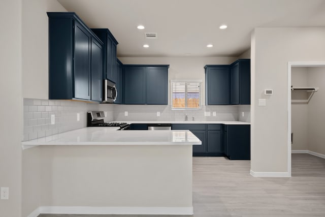 kitchen with appliances with stainless steel finishes, tasteful backsplash, sink, kitchen peninsula, and light wood-type flooring