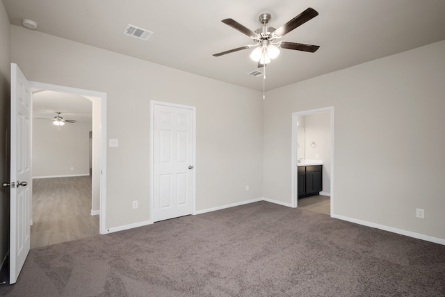 unfurnished bedroom with dark colored carpet, ceiling fan, and ensuite bath