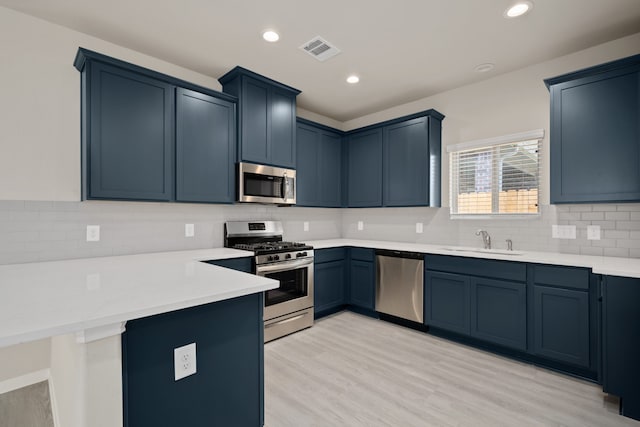 kitchen with sink, appliances with stainless steel finishes, blue cabinets, decorative backsplash, and light wood-type flooring