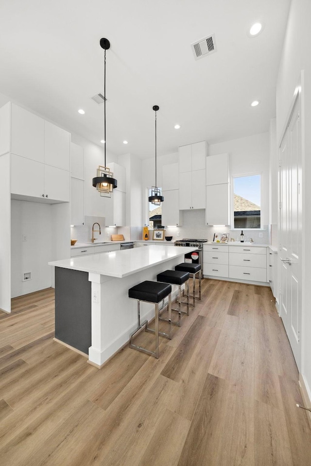 kitchen featuring white cabinetry, a breakfast bar area, hanging light fixtures, a center island, and light hardwood / wood-style floors