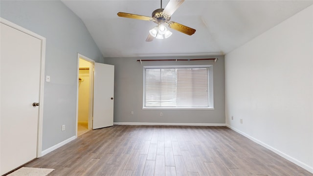 unfurnished bedroom featuring lofted ceiling, a spacious closet, ceiling fan, light wood-type flooring, and baseboards