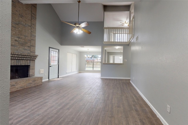 unfurnished living room featuring visible vents, a brick fireplace, wood finished floors, baseboards, and ceiling fan with notable chandelier