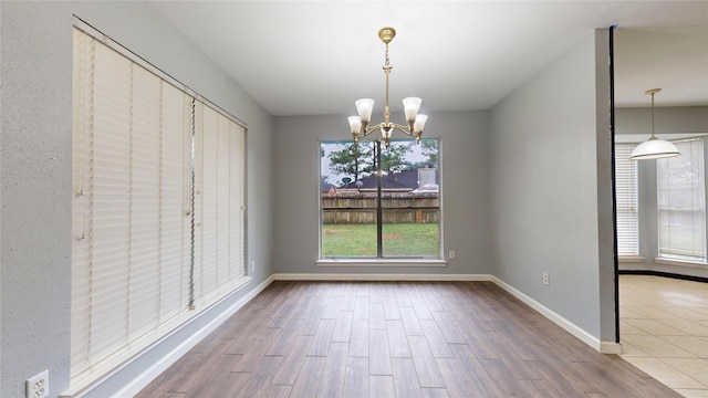 unfurnished dining area with baseboards, a notable chandelier, and wood finished floors