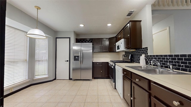 kitchen with stainless steel appliances, light countertops, a sink, and decorative light fixtures