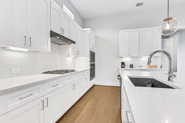 kitchen with sink, decorative light fixtures, appliances with stainless steel finishes, light hardwood / wood-style floors, and white cabinets