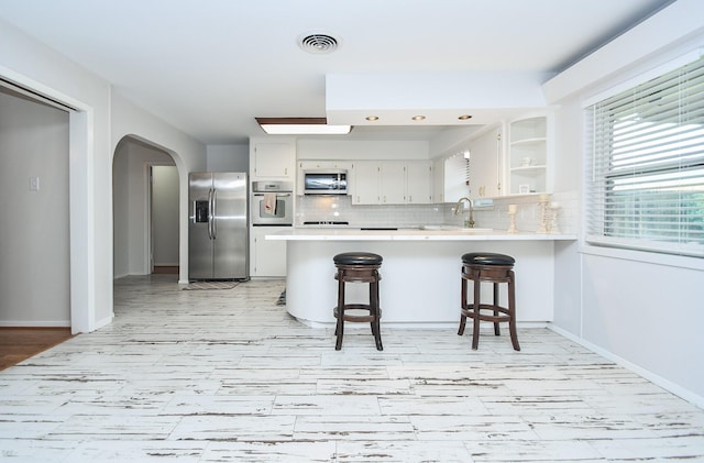 kitchen with white cabinetry, stainless steel appliances, a kitchen bar, and kitchen peninsula