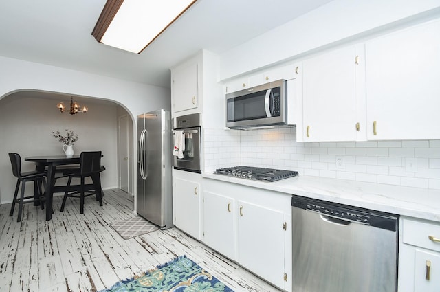 kitchen featuring appliances with stainless steel finishes, white cabinetry, backsplash, a notable chandelier, and light stone counters