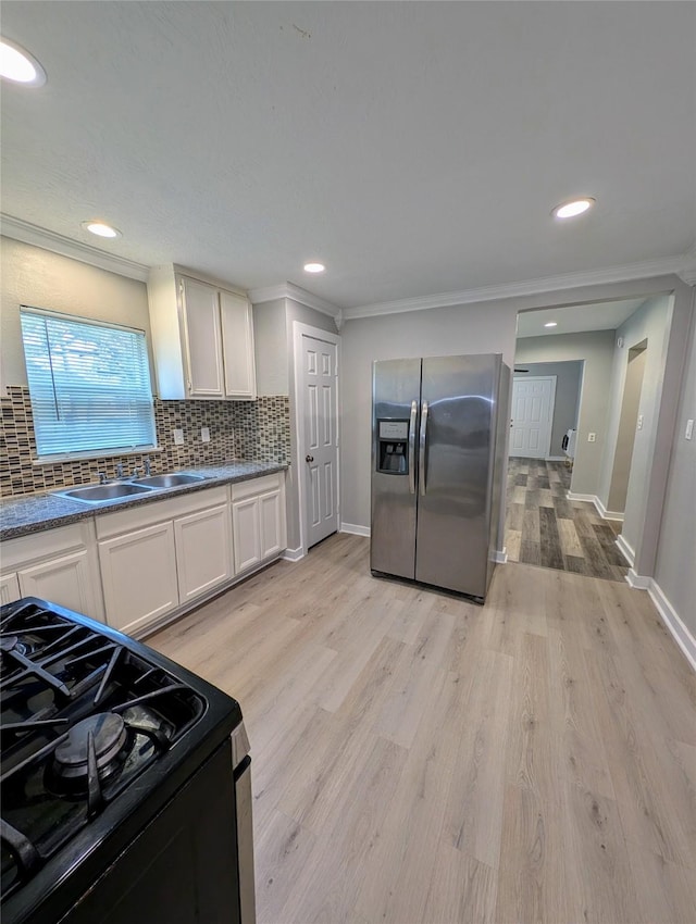 kitchen with sink, gas range, stainless steel fridge with ice dispenser, white cabinets, and backsplash