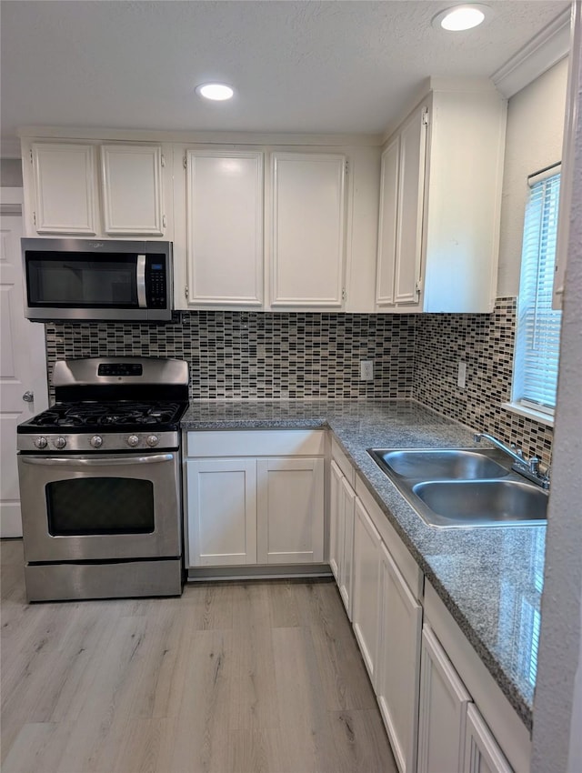 kitchen with sink, light hardwood / wood-style flooring, stainless steel appliances, decorative backsplash, and white cabinets