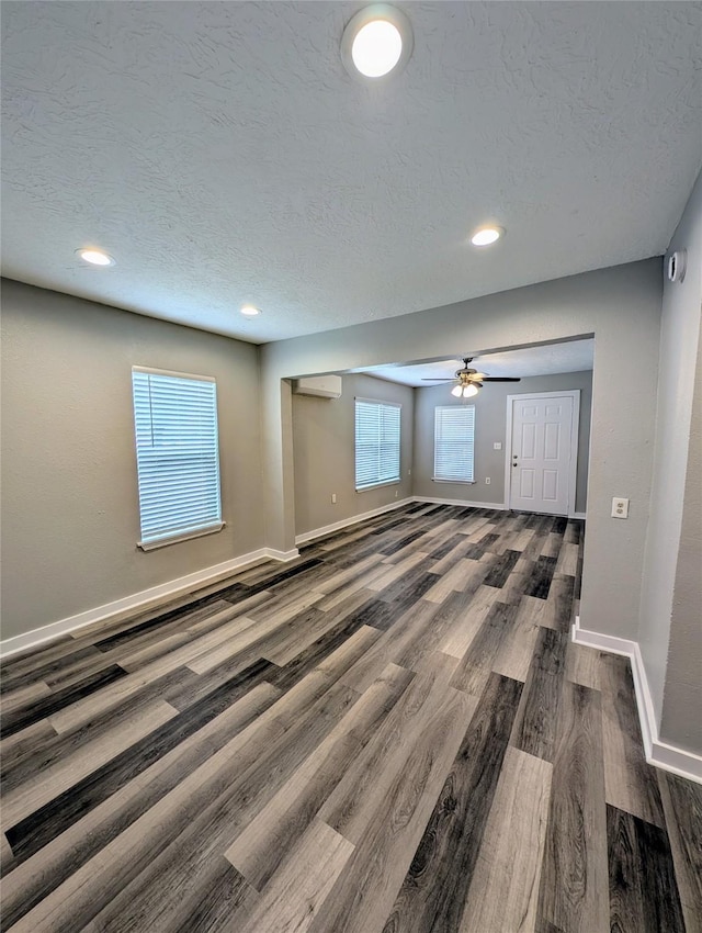 unfurnished living room featuring dark hardwood / wood-style flooring, ceiling fan, a wall mounted AC, and a textured ceiling