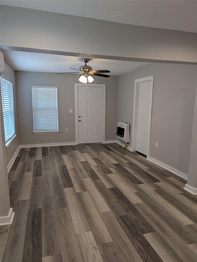 unfurnished living room featuring heating unit, a textured ceiling, dark wood-type flooring, and ceiling fan