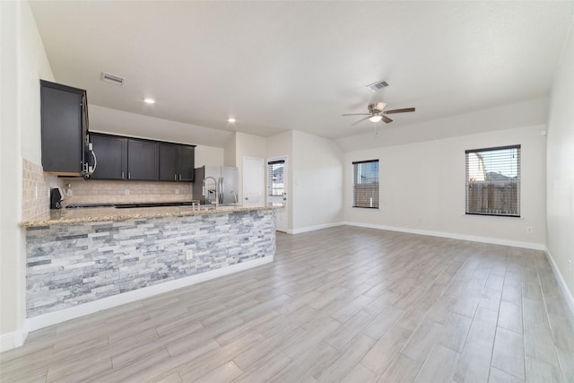 kitchen featuring ceiling fan, range, backsplash, stainless steel refrigerator with ice dispenser, and light stone counters