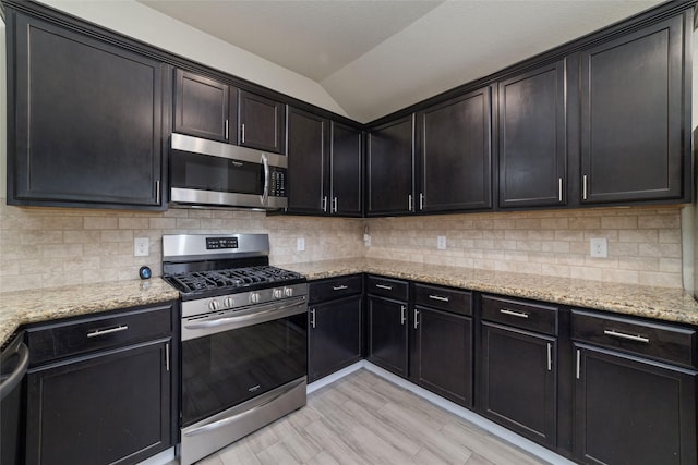 kitchen featuring vaulted ceiling, appliances with stainless steel finishes, tasteful backsplash, light stone counters, and light hardwood / wood-style floors