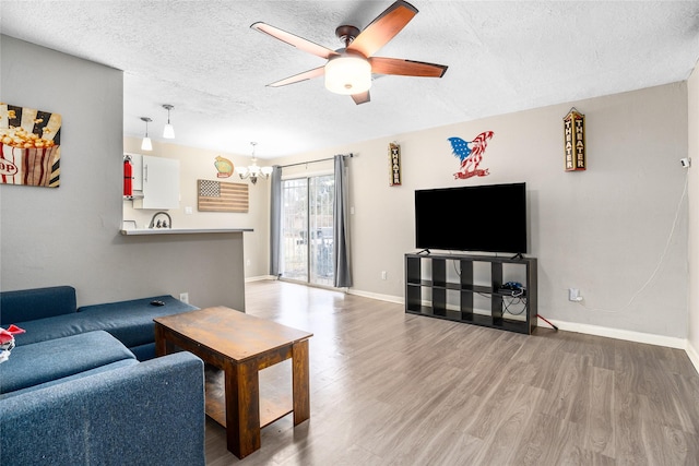 living room with ceiling fan with notable chandelier, wood-type flooring, and a textured ceiling