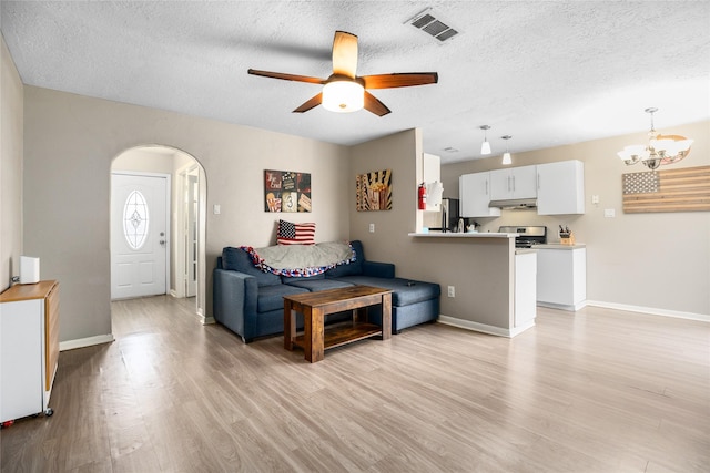 living room with ceiling fan with notable chandelier, a textured ceiling, and light hardwood / wood-style floors