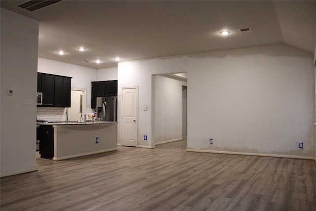 kitchen with vaulted ceiling, appliances with stainless steel finishes, tasteful backsplash, hardwood / wood-style flooring, and a center island with sink