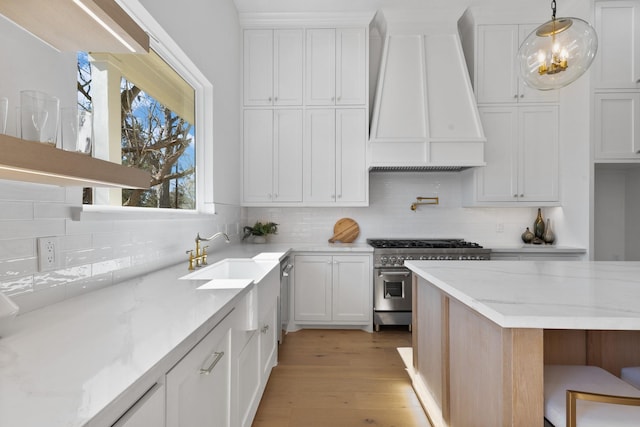 kitchen with stainless steel stove, premium range hood, white cabinetry, light stone counters, and decorative light fixtures