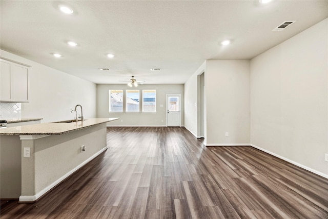 kitchen with dark hardwood / wood-style floors, sink, decorative backsplash, light stone countertops, and a center island with sink