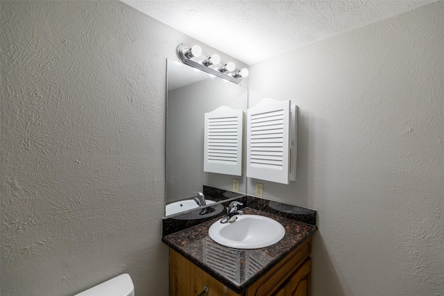 bathroom featuring a textured ceiling, toilet, vanity, and a textured wall