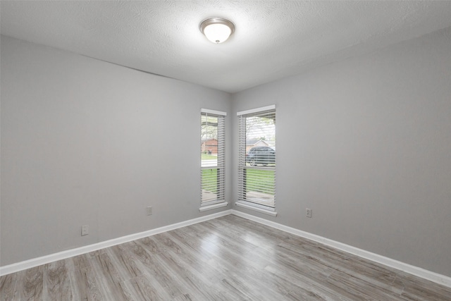 spare room featuring light wood-type flooring, baseboards, and a textured ceiling