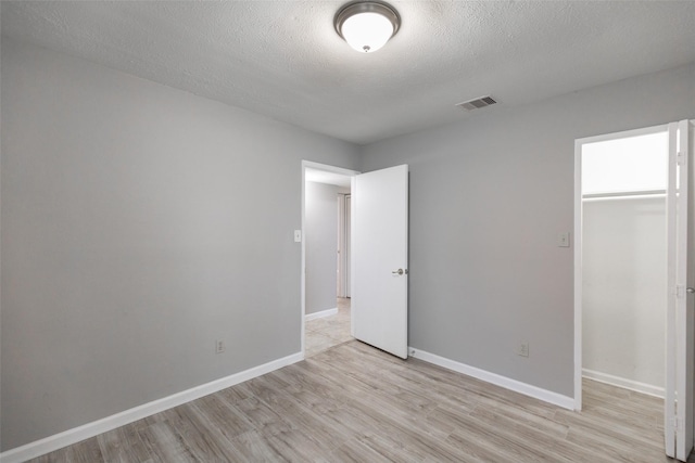 unfurnished bedroom featuring visible vents, a textured ceiling, a closet, light wood-style floors, and baseboards