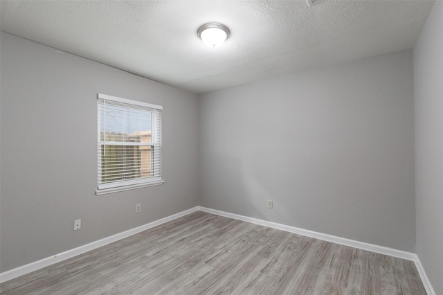 unfurnished room featuring baseboards, light wood finished floors, and a textured ceiling