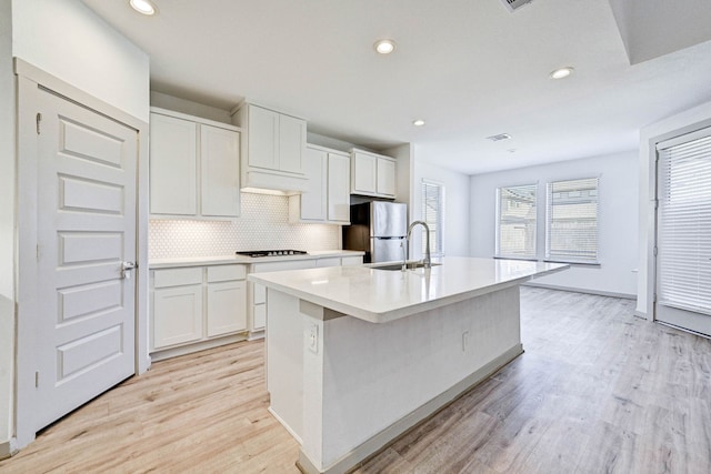 kitchen featuring a kitchen island with sink, white cabinets, stainless steel refrigerator, and light hardwood / wood-style floors