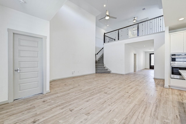 unfurnished living room with a towering ceiling, ceiling fan, and light hardwood / wood-style flooring