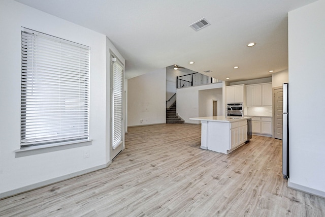 kitchen featuring appliances with stainless steel finishes, white cabinetry, a wealth of natural light, light hardwood / wood-style floors, and a center island with sink