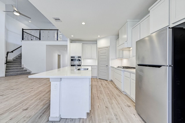 kitchen featuring light hardwood / wood-style flooring, backsplash, stainless steel appliances, white cabinets, and a center island with sink