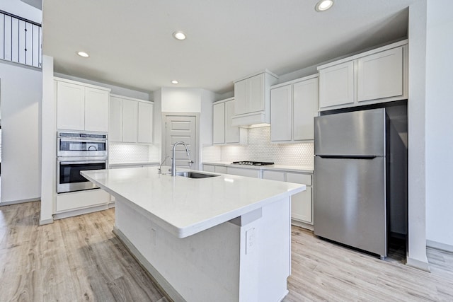 kitchen with appliances with stainless steel finishes, white cabinetry, sink, decorative backsplash, and a center island with sink