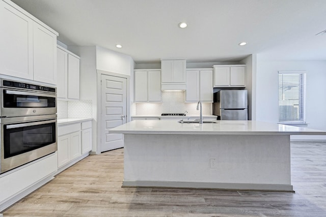 kitchen with white cabinetry, an island with sink, sink, stainless steel appliances, and light hardwood / wood-style flooring