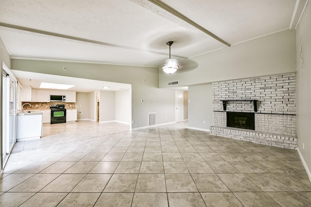 unfurnished living room with sink, ceiling fan, vaulted ceiling with beams, a fireplace, and light tile patterned flooring